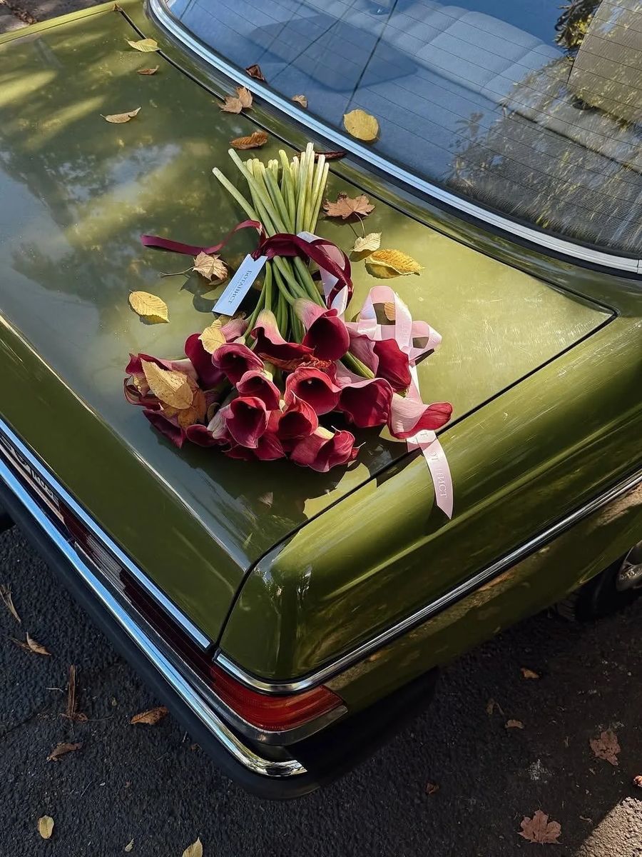 Autumn calla bouquet — delivery in Istanbul A bouquet of deep burgundy calla lilies with a wine silk ribbon on the trunk of an olive vintage car amid autumn leaves