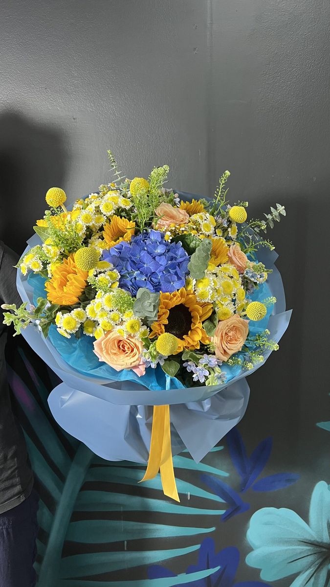 A bright summer bouquet with blue hydrangea, sunflowers, craspedia and chamomile in blue wrapping — Antalya